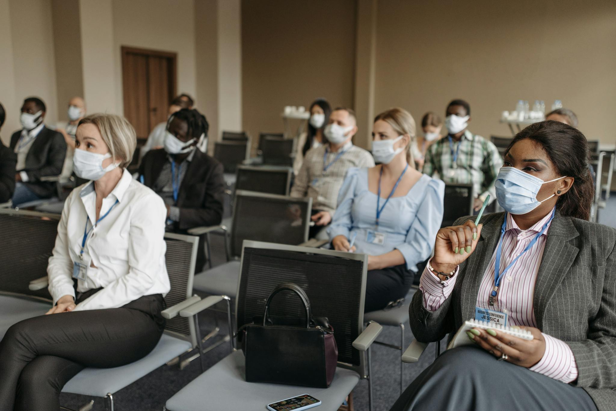 Diverse group of professionals in a conference room wearing face masks during a business seminar.
