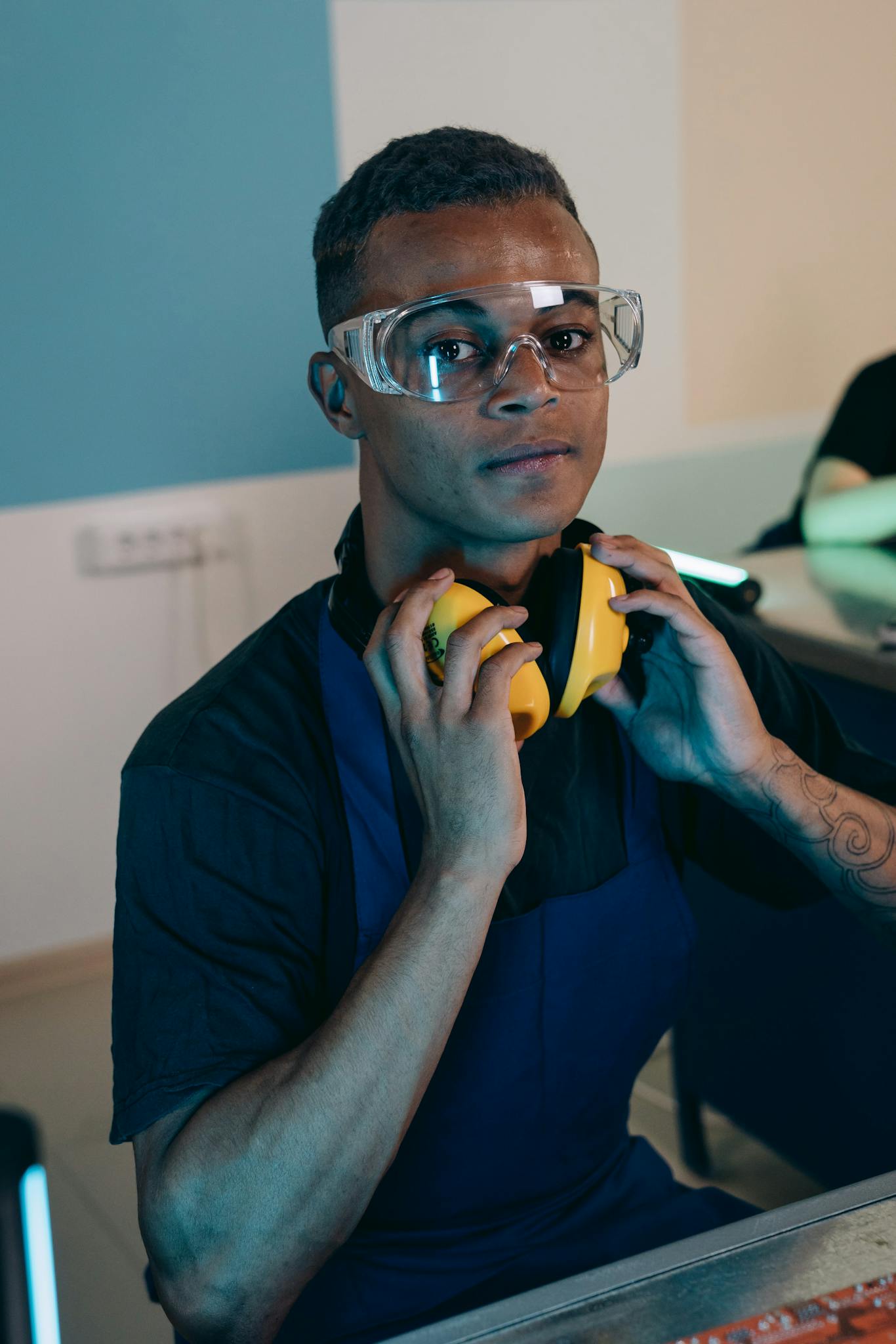Portrait of a young engineer wearing safety glasses and headphones in a workspace.